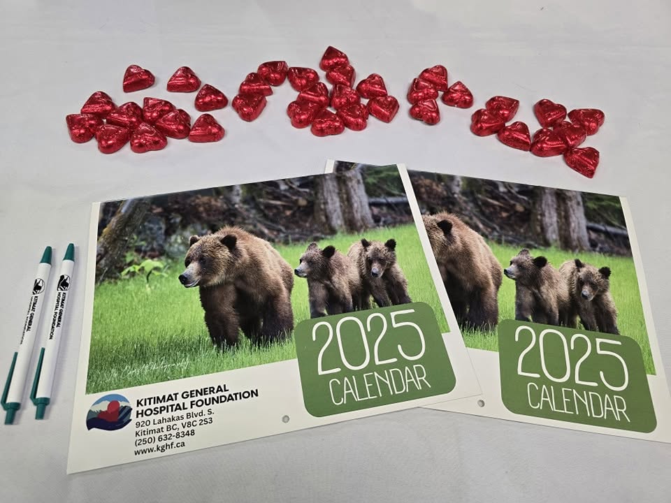 Two KGHF 2025 calendars with a grizzly bear and cubs on the cover, beside KGHF pens and red foil heart chocolates